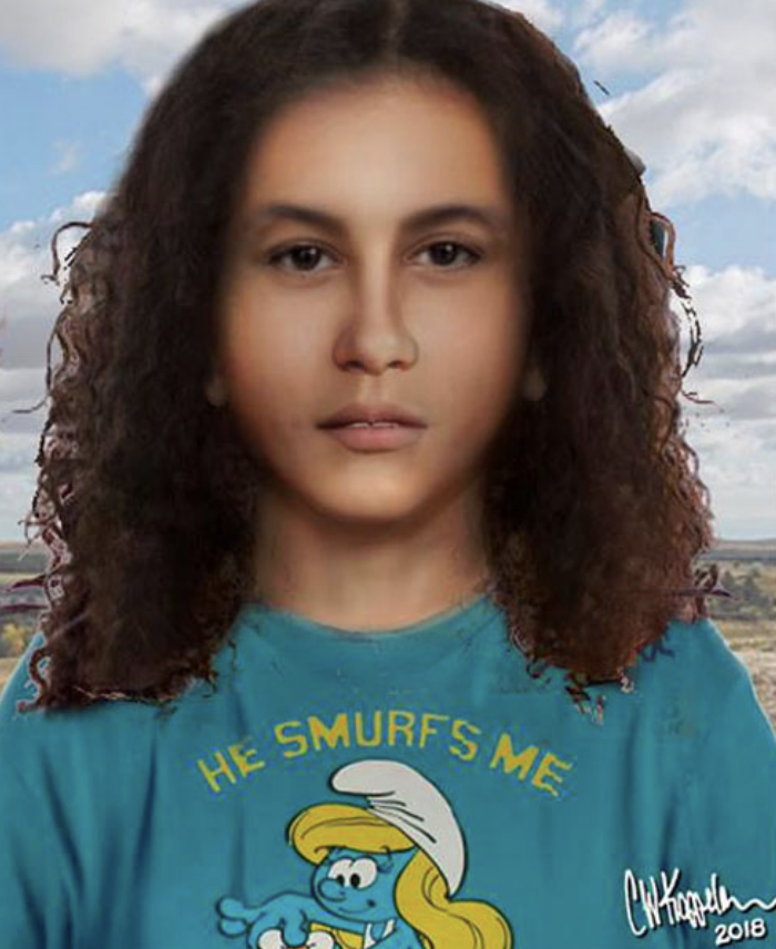 A person with long, curly hair wearing a blue "He Smurfs Me" shirt with a graphic of Smurfette on it. There's a landscape view in the background