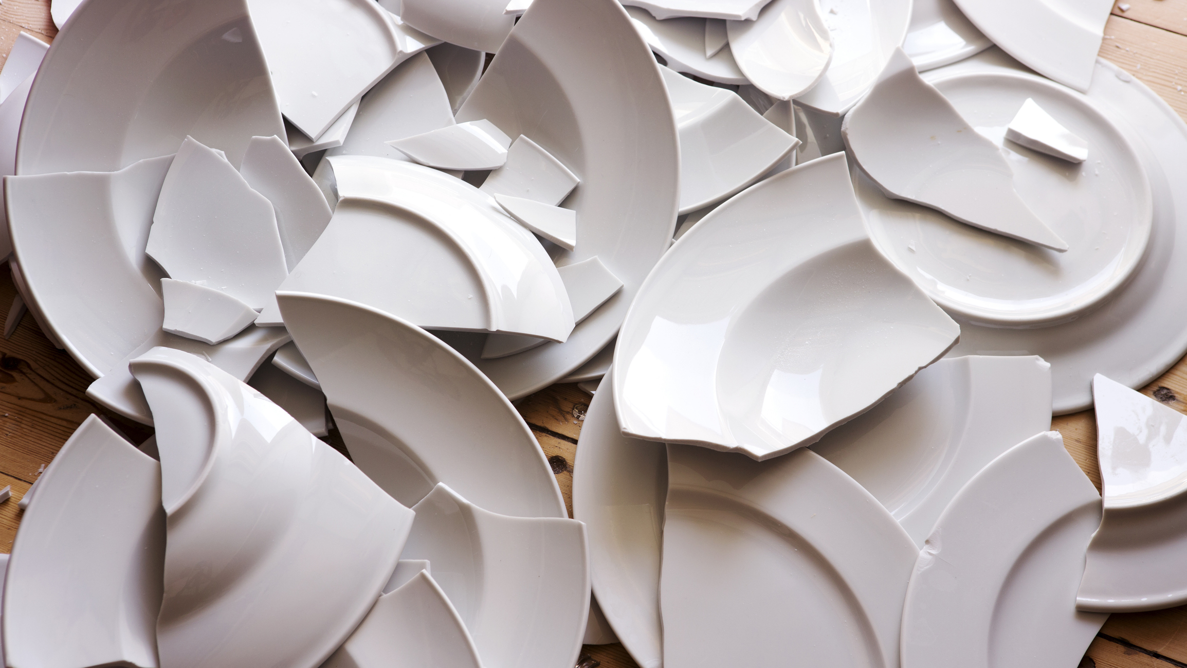 Pile of broken white plates scattered over a wooden surface