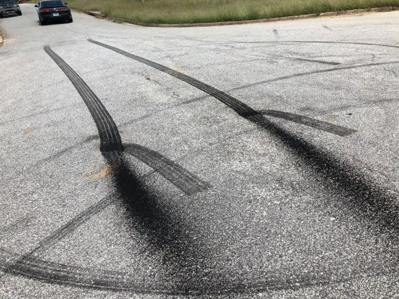 Street with tire skid marks extending in curved patterns, suggesting recent car activity. Two cars are parked at a distance. No people are visible