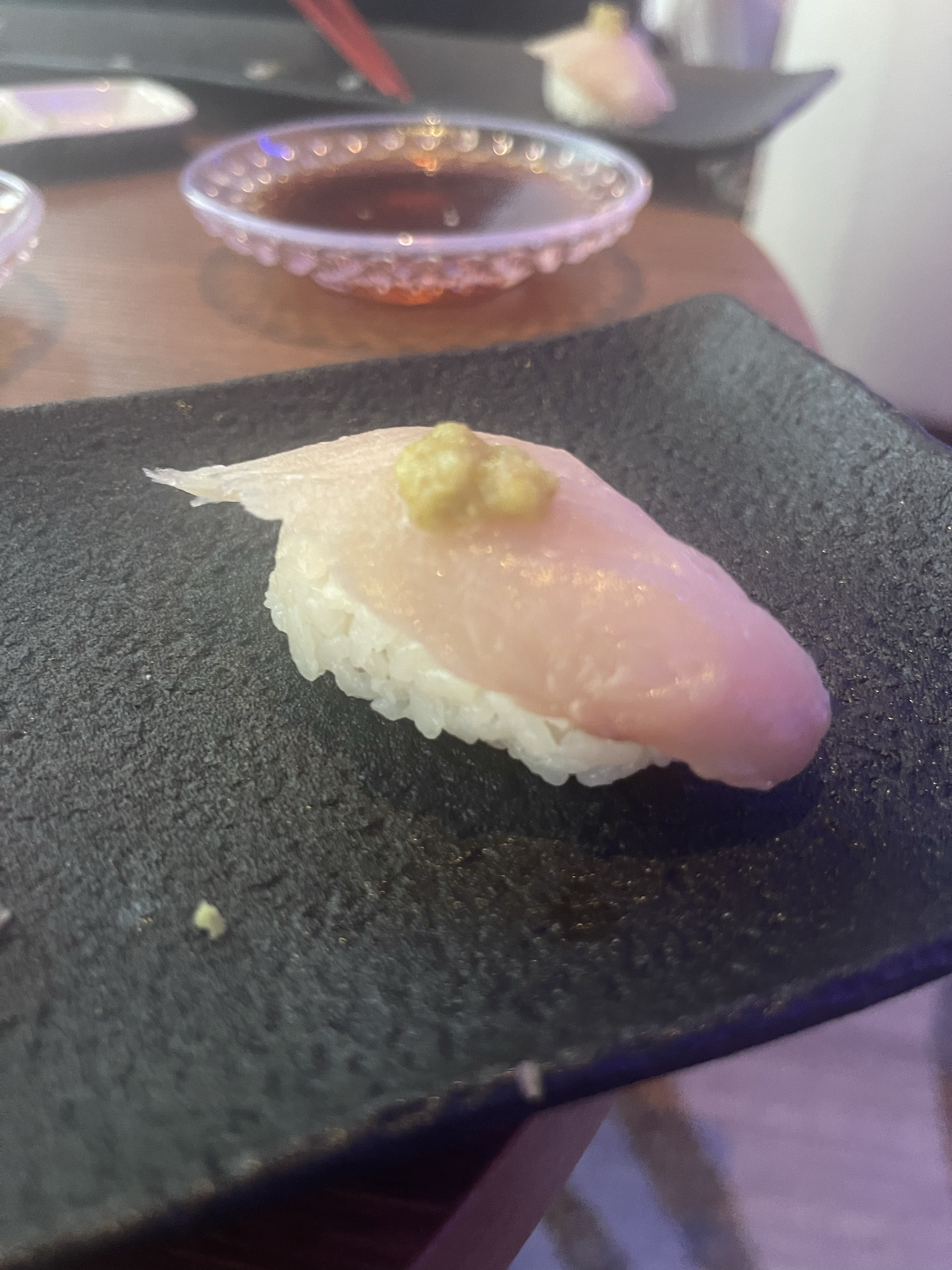 Close-up of a piece of sushi with a slice of fish on top of rice, garnished with a small amount of wasabi, on a dark plate