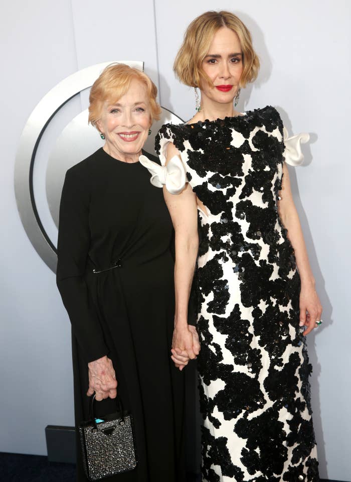 Holland Taylor and Sarah Paulson on a red carpet. Holland wears a long black dress, while Sarah wears a black and white patterned gown with floral accents