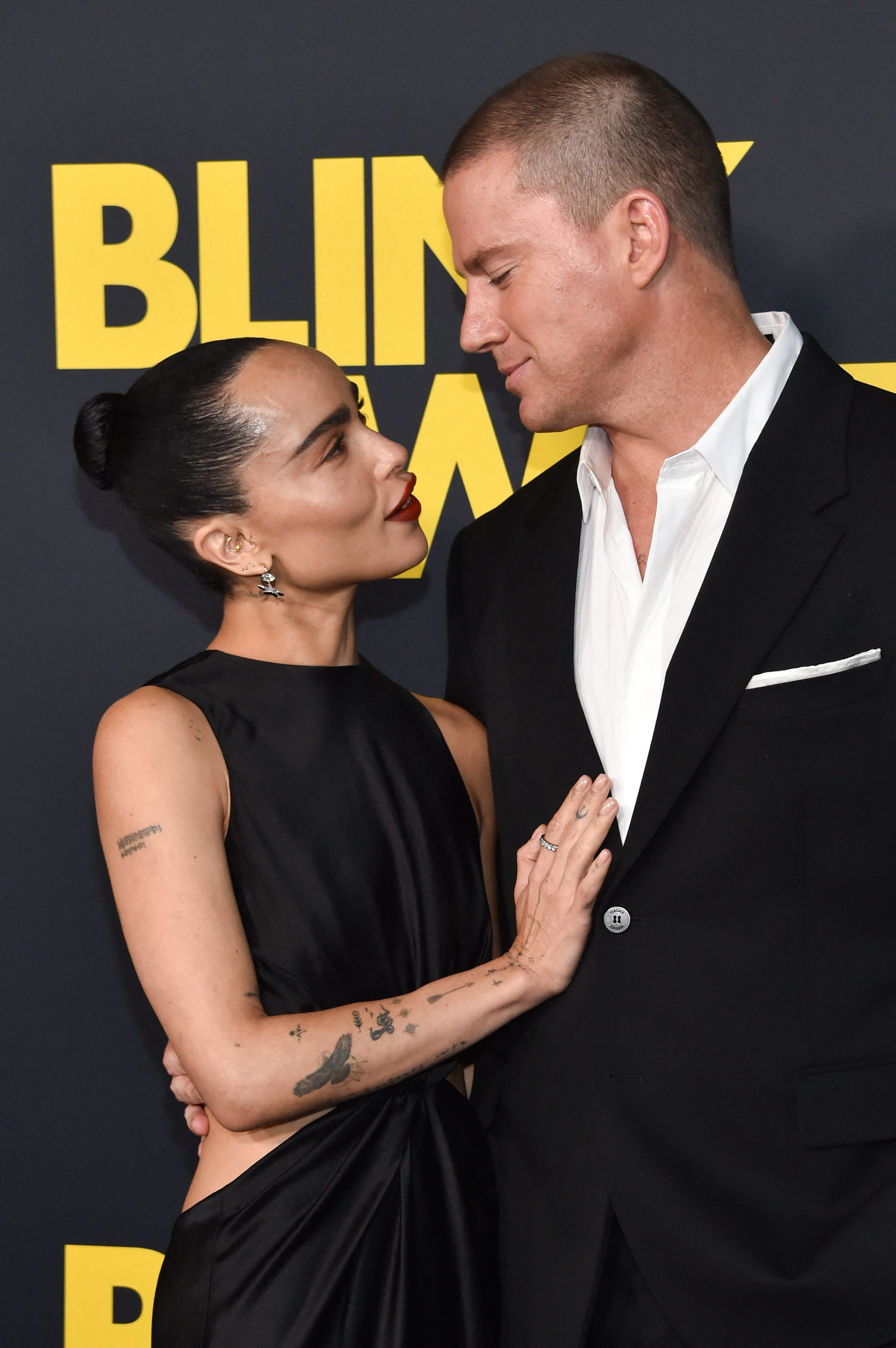 Zoe Kravitz in a sleek, sleeveless black dress and Channing Tatum in a classic black suit and white shirt, smiling and embracing on a red carpet