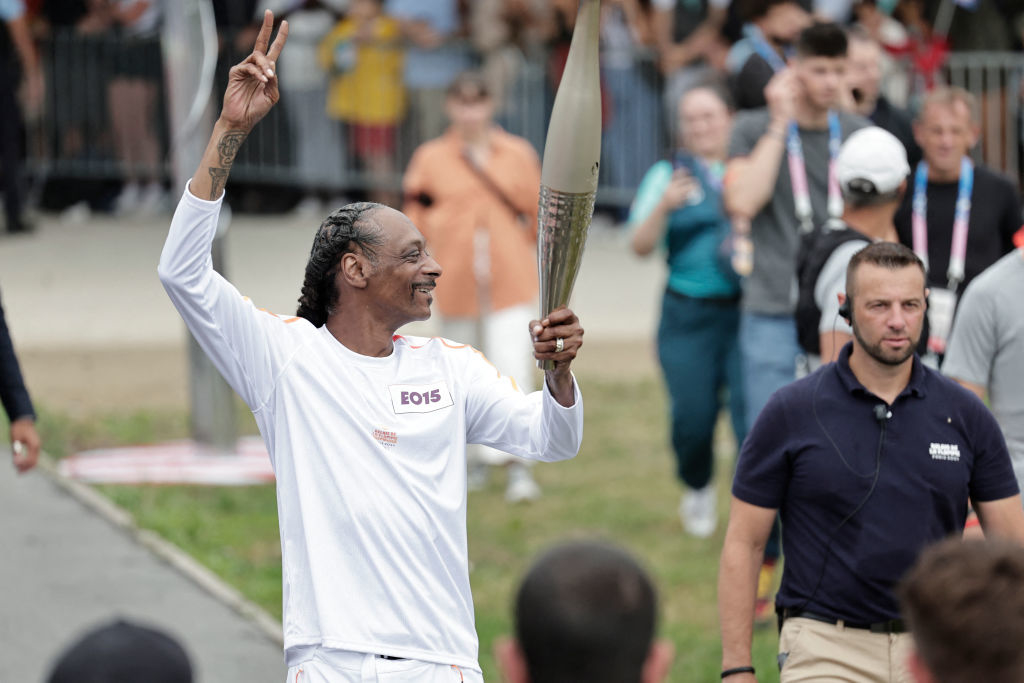 Snoop Dogg holds a torch and flashes a peace sign at the Olympics