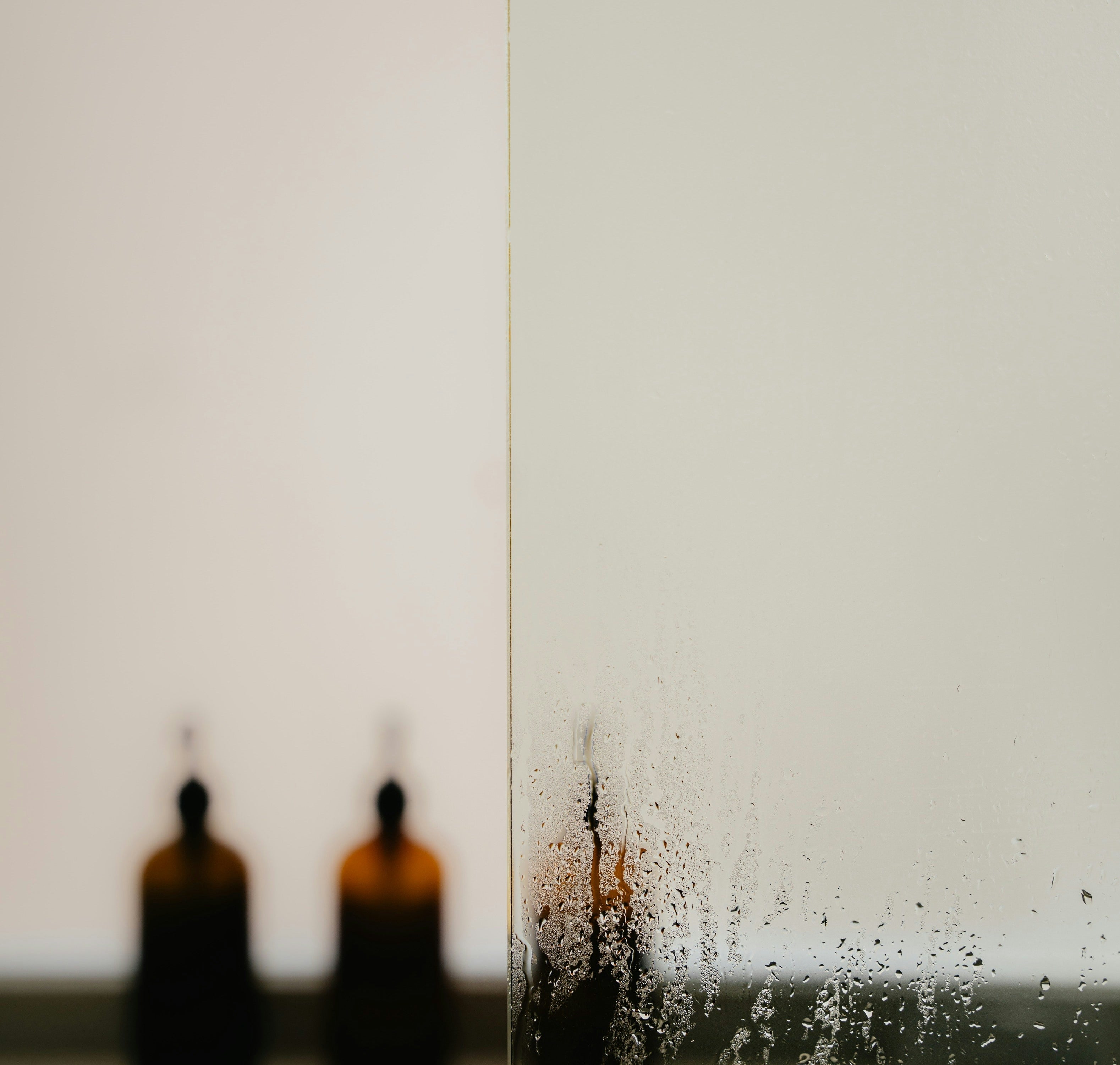 Moist, foggy glass panel partially revealing blurred brown bottles on a shelf in the background. No people present