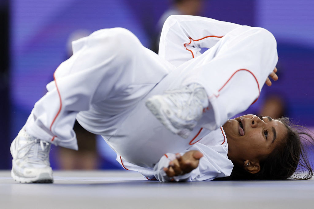 B-girl India performs a contorting breakdancing move, wearing a outfit with accents, during a competition