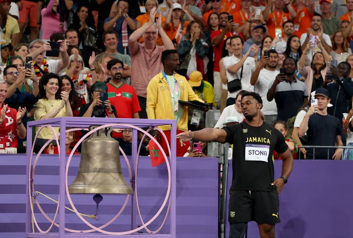 Jamaica’s Andrew Hudson rings a bell on the track, surrounded by cheering fans in the stands