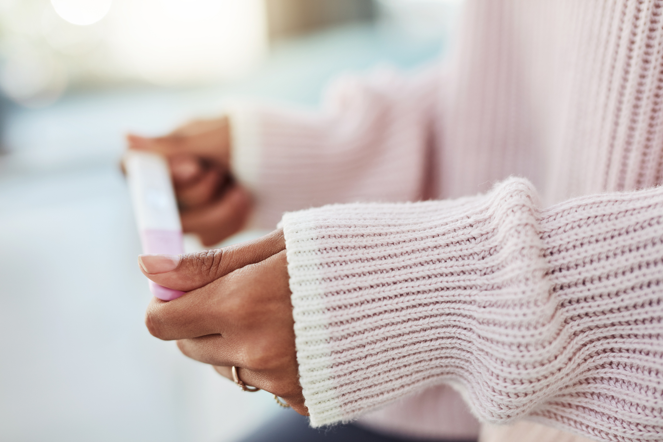 Person in a knit sweater holding a pregnancy test