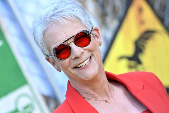 Jamie Lee Curtis smiling, wearing red sunglasses and a red blazer