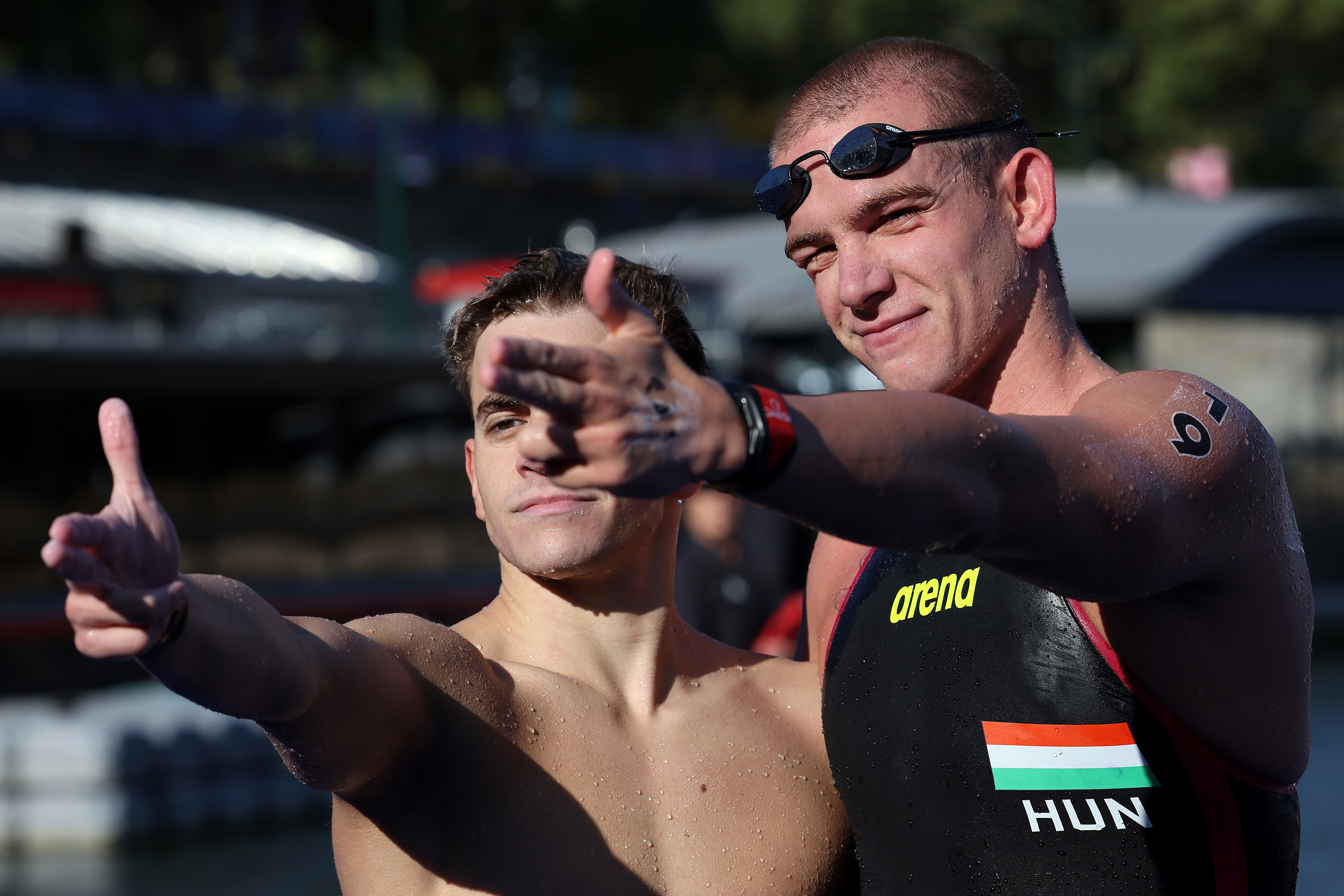 Kristof Rasovszky and another swimmer at an outdoor venue in swim gear, gesturing towards the camera