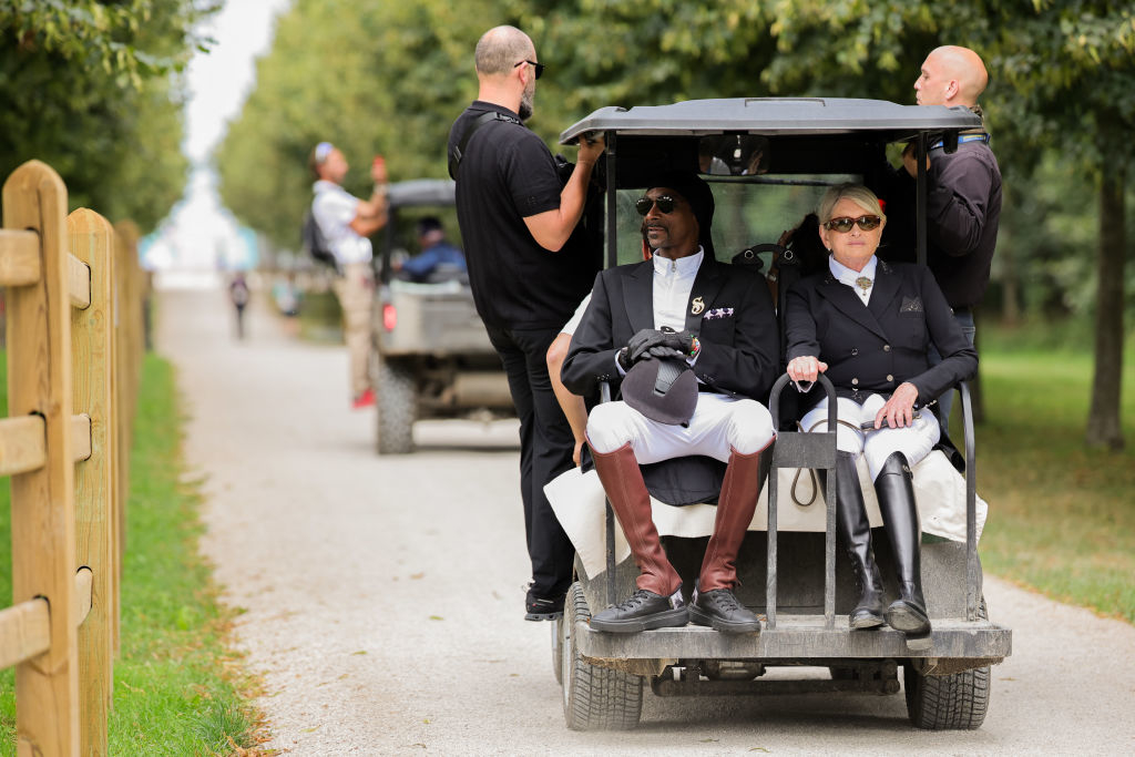 Snoop Dogg and Martha Stewart ride in a golf cart, surrounded by security personnel dressed in equestrian outfits