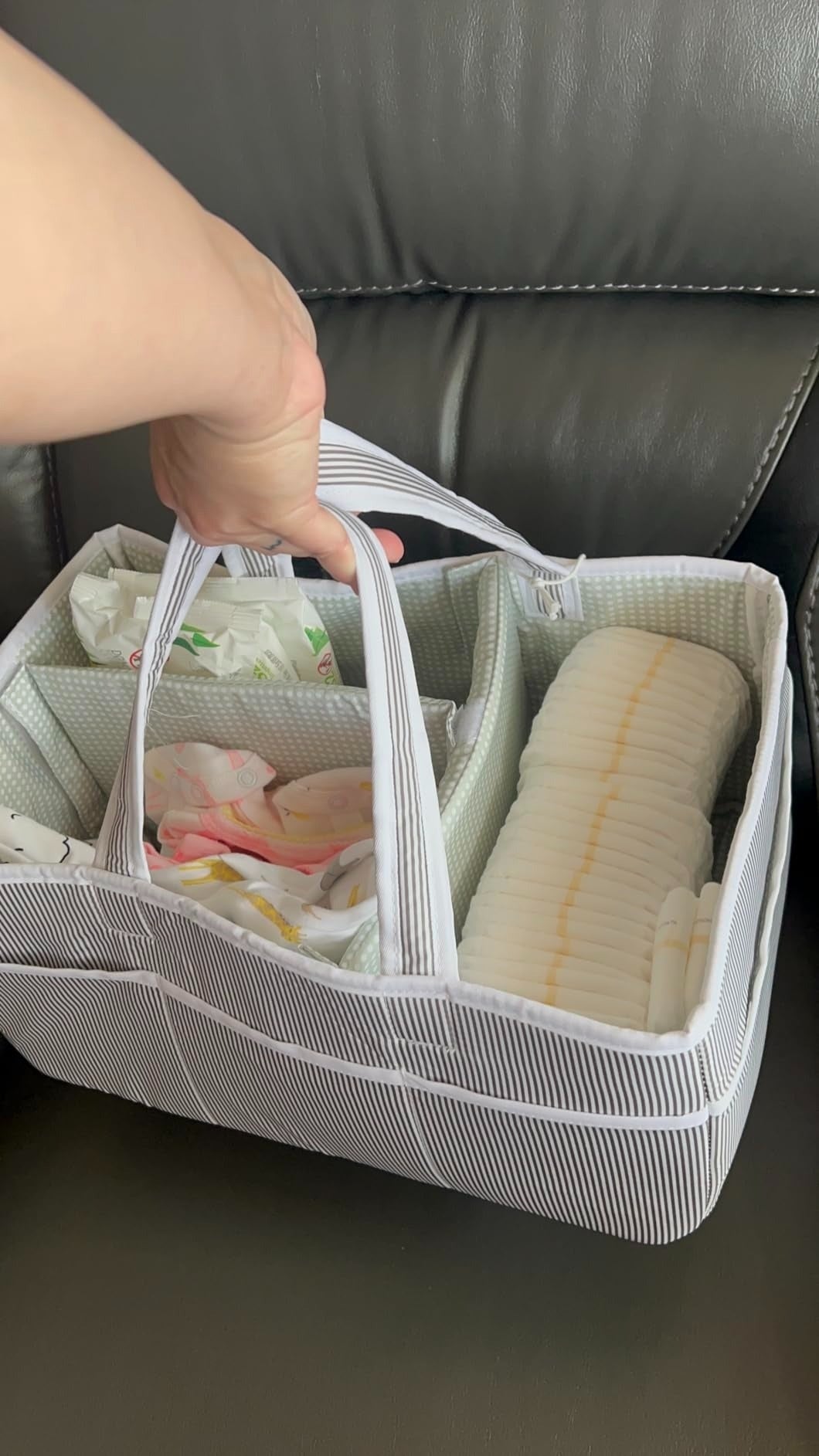 A manus  holding a striped organizer handbasket  filled with babe  diapers and packaged babe  wipes. The handbasket  has respective  compartments for casual  storage