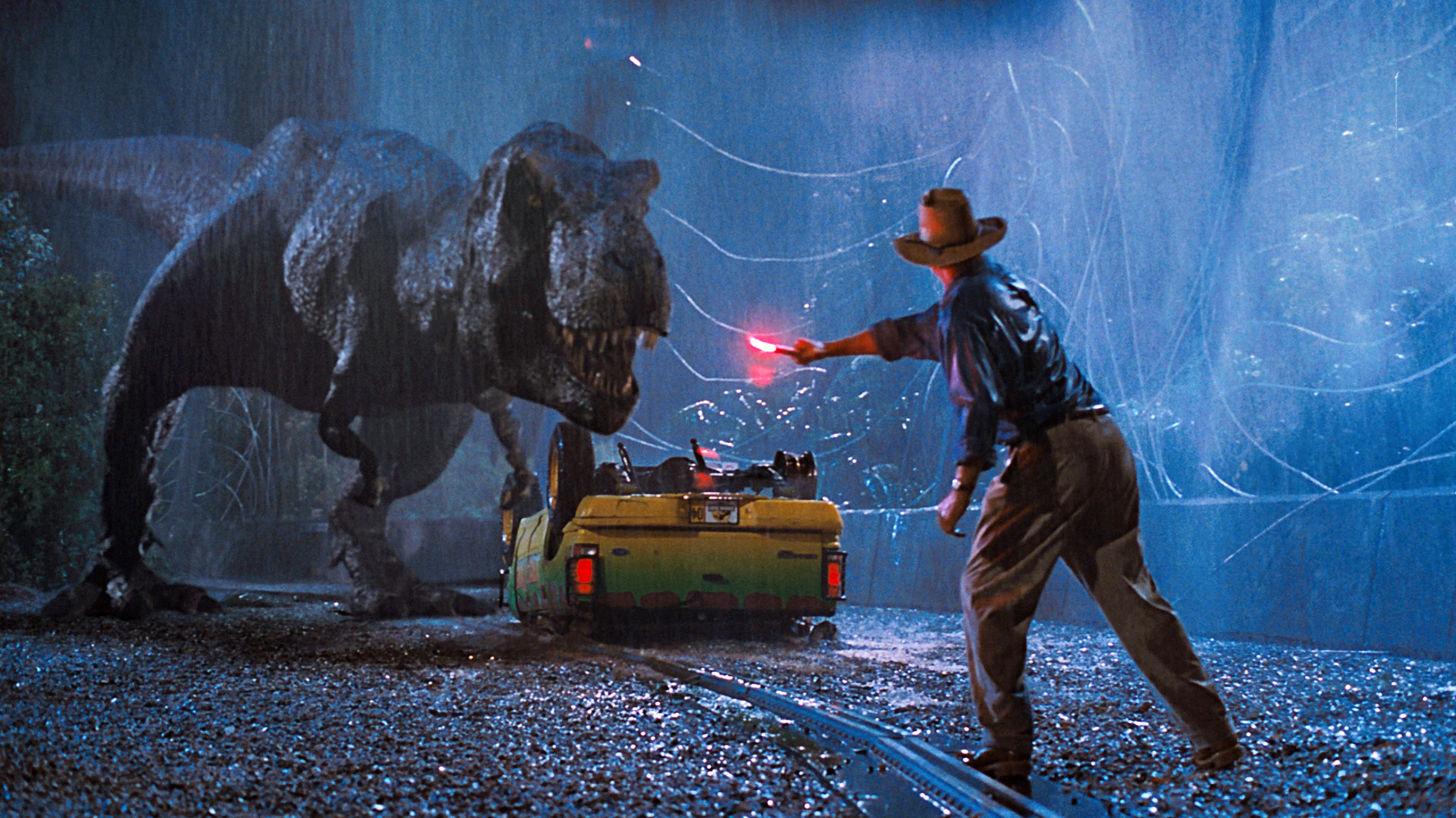 Dr. Grant holding a flare in front of a T-Rex and overturned car