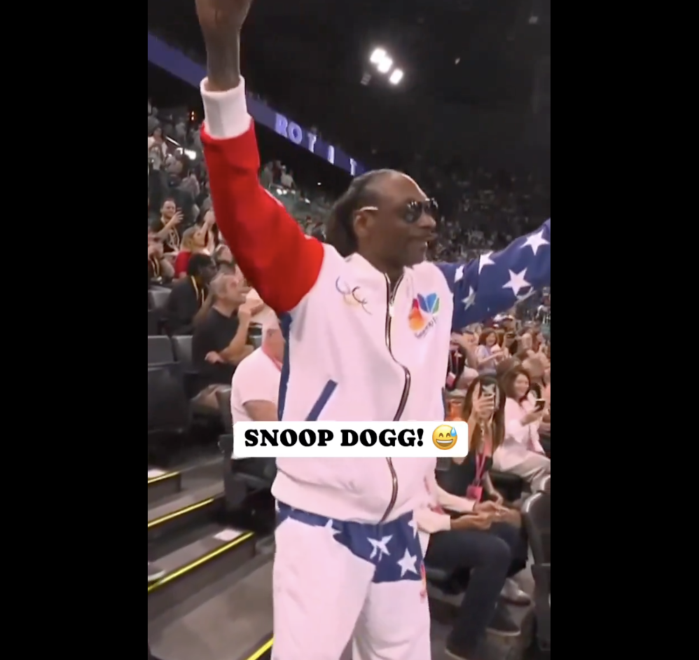 Snoop Dogg, wearing a white tracksuit with red, blue, and star designs, raising his arms and celebrating with Simone Biles