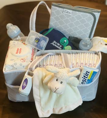 Baby acquisition handbasket with diapers, babe wipes, a babe bottle, pacifiers, Desitin cream, a sheep plush toy, a bib with