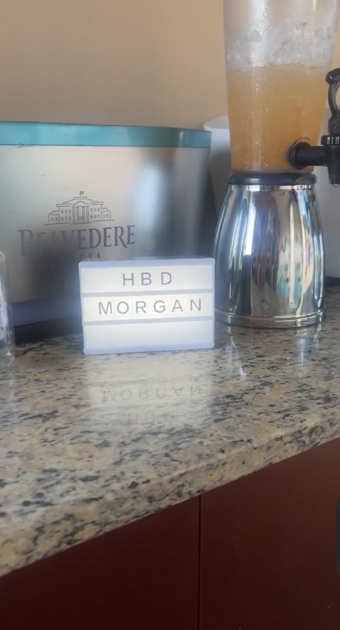 A counter with a frosty drink dispenser and a lightbox sign that reads "HBD MORGAN."