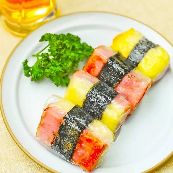 四角い寿司が白い皿に4個、左にパセリ、後ろに飲み物が見えます。