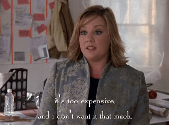 Melissa McCarthy in an office setting, saying, &quot;It's too expensive, and I don't want it that much,&quot; from a scene in a movie or TV show. Desk with notes and a water bottle in the background