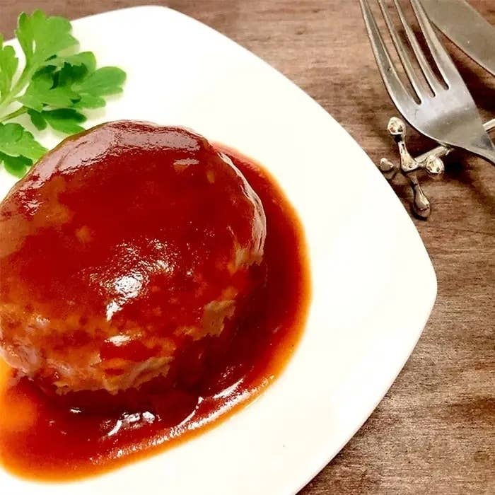 白い皿にのったデミグラスソースがかかったハンバーグと、左上に置かれたパセリの飾り。右側にナイフとフォークが置かれています。