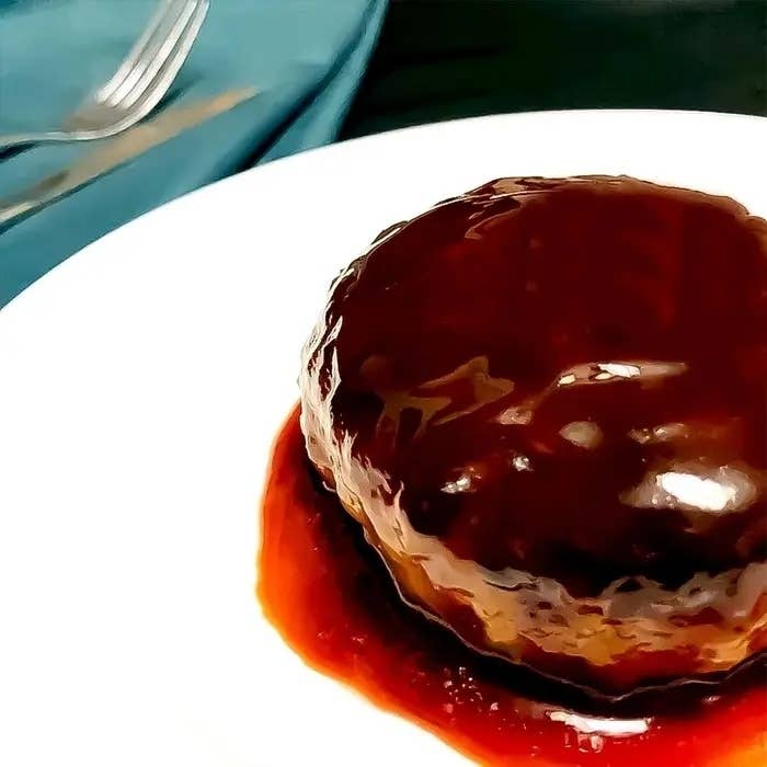 白い皿にのったデミグラスソースのハンバーグ。背景に銀色のフォーク。