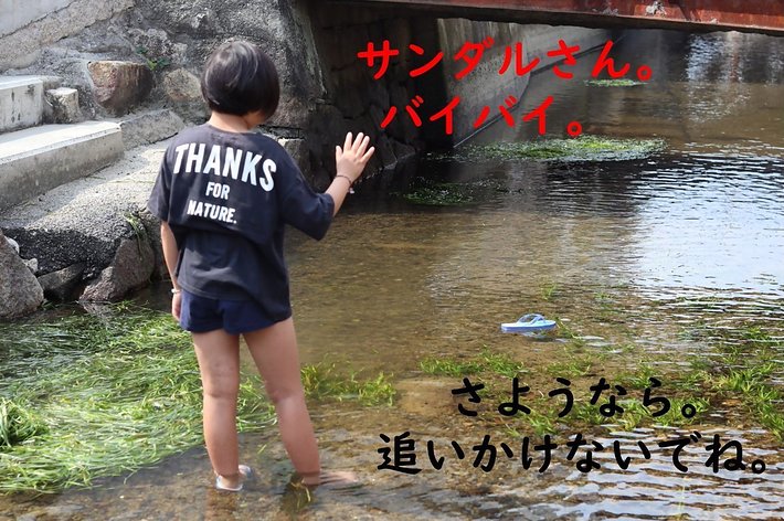 子供が川でサンダルにさよならを言う。背中のシャツには「THANKS FOR NATURE」の文字が書かれている。