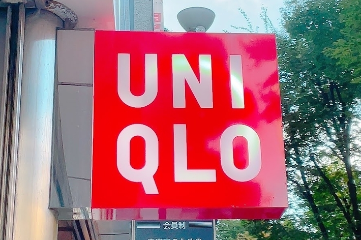 A red and white UNIQLO store sign is mounted outside on a building with trees visible in the background