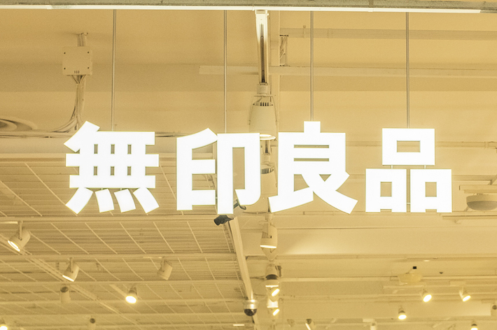 A Muji store with customers browsing through various products. The sign above is in Japanese, indicating the store’s name. The interior is minimalist and organized