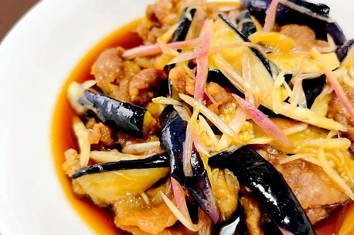 皿に盛られた揚げなすと肉の餡かけ料理。生姜の千切りが上に散らされている。