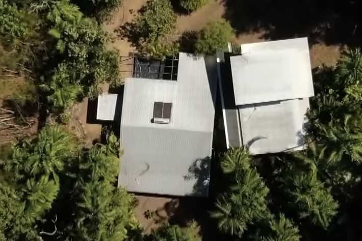 上から見た家の航空写真。家は森林に囲まれています。ニュースチャンネルのロゴが表示されています。