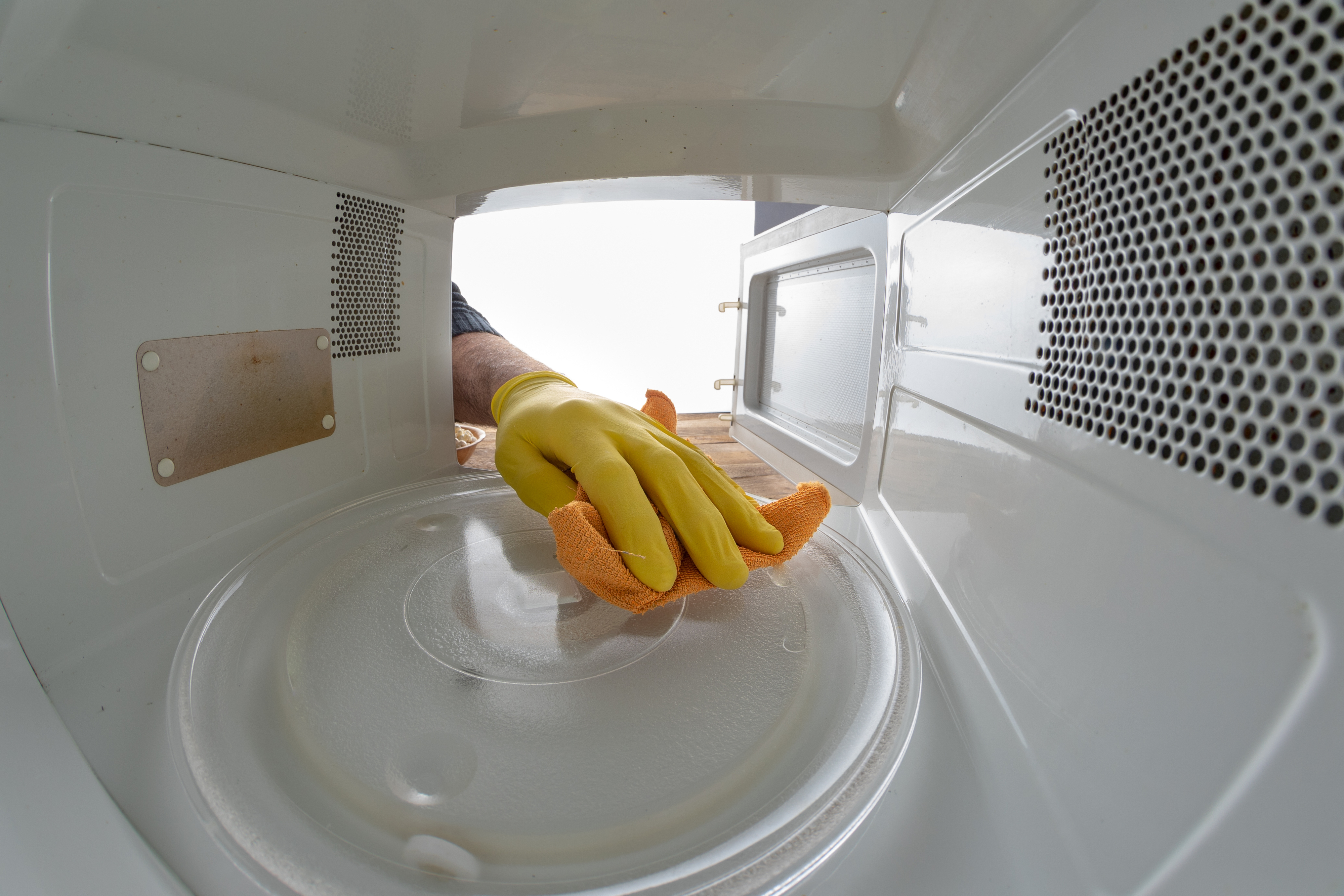 Person wearing rubber gloves cleaning the interior of a microwave with an orange cloth
