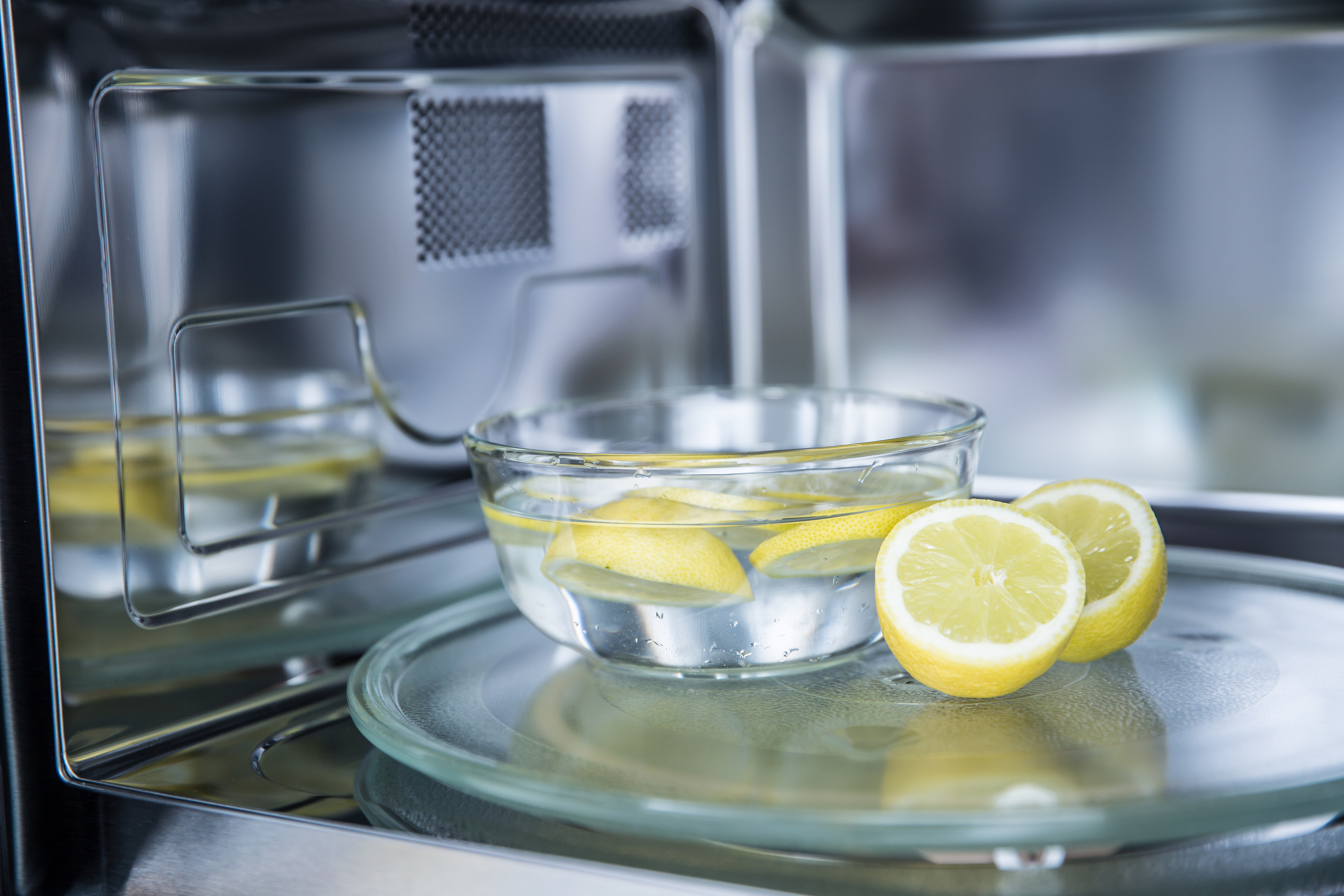 Microwave with a glass bowl of water and lemon slices on a turntable, set up for cleaning or deodorizing the appliance