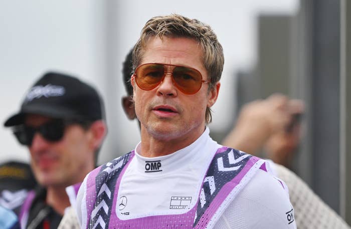 Brad Pitt, wearing a racing jumpsuit with geometric patterns and large aviator sunglasses, attends a public event