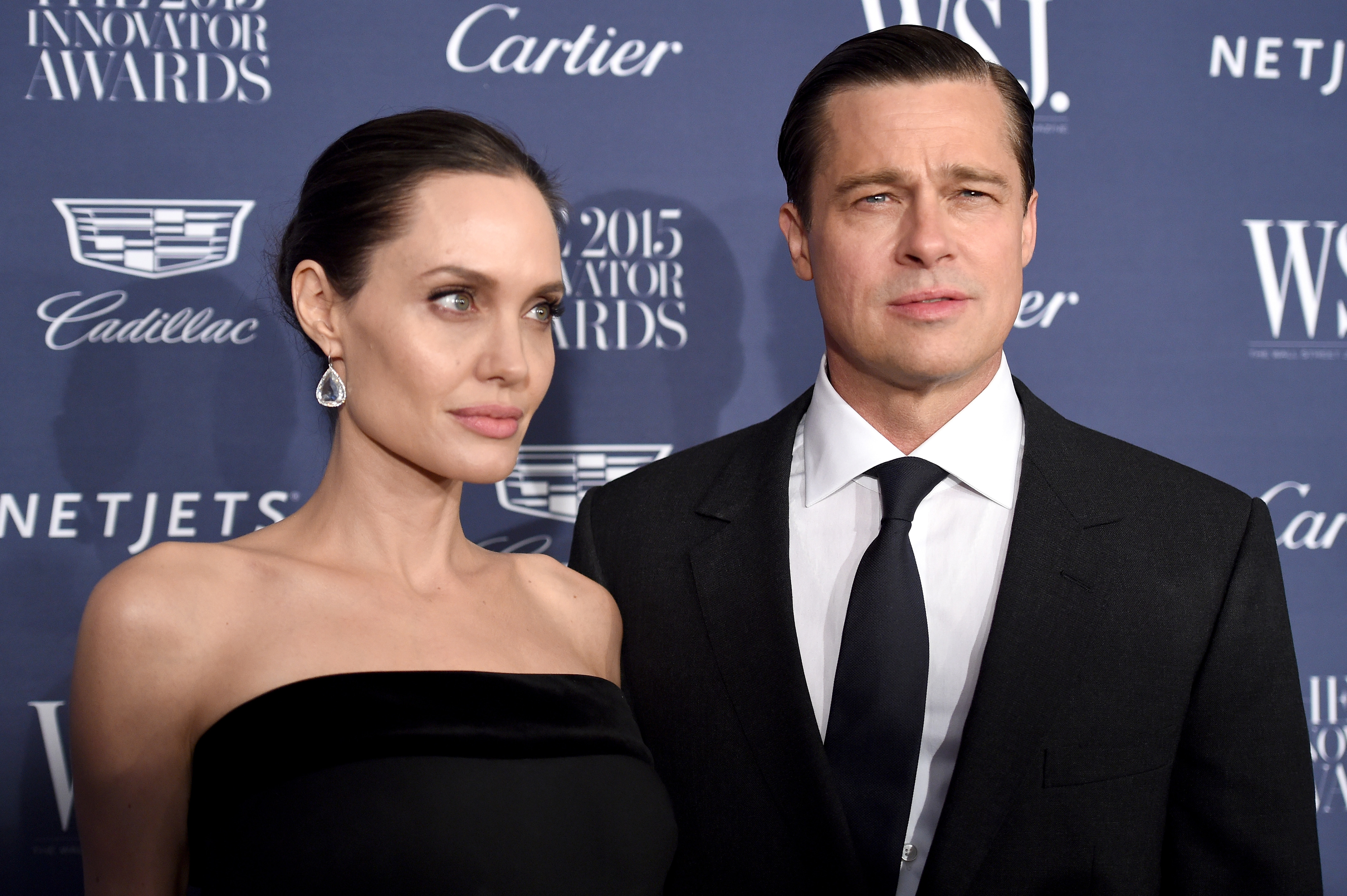 Angelina Jolie and Brad Pitt at the WSJ Innovator Awards. Angelina wears a strapless black dress with drop earrings, and Brad wears a black suit with a tie