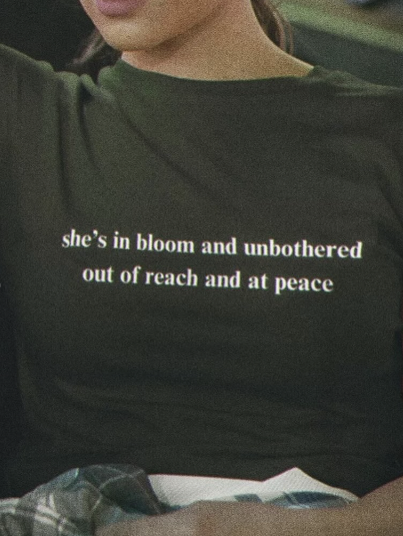 A person wearing a shirt that says, "she's in bloom and unbothered out of reach and at peace."