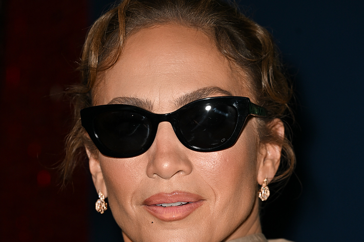 Jennifer Lopez wearing  sunglasses, gold earrings, and a high-collared outfit