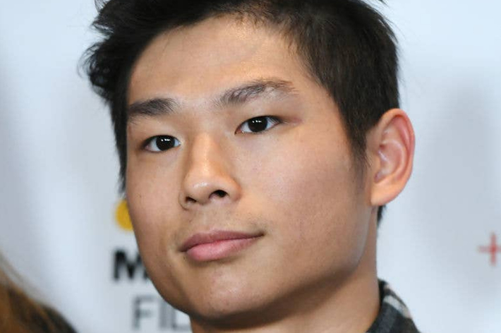 A person stands in front of a backdrop at an event, wearing casual clothing