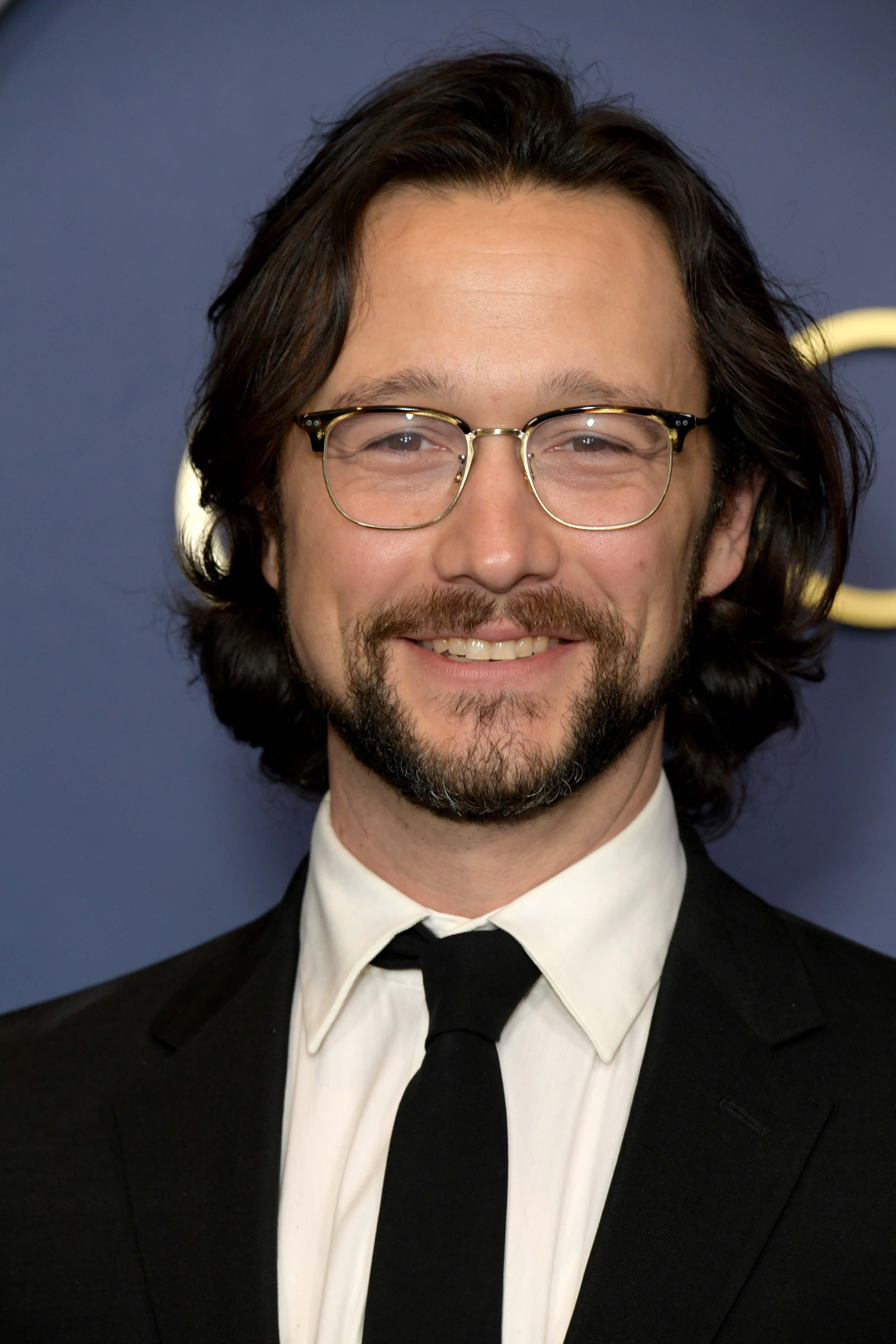 Joseph Gordon-Levitt smiles at the camera, wearing a suit and tie at a formal event