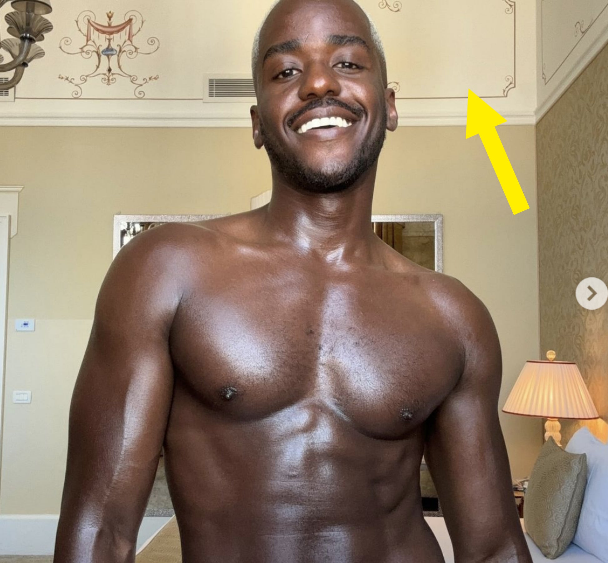 Ncuti Gatwa smiling, shirtless, and wearing a towel in a luxurious hotel room with ornate decor