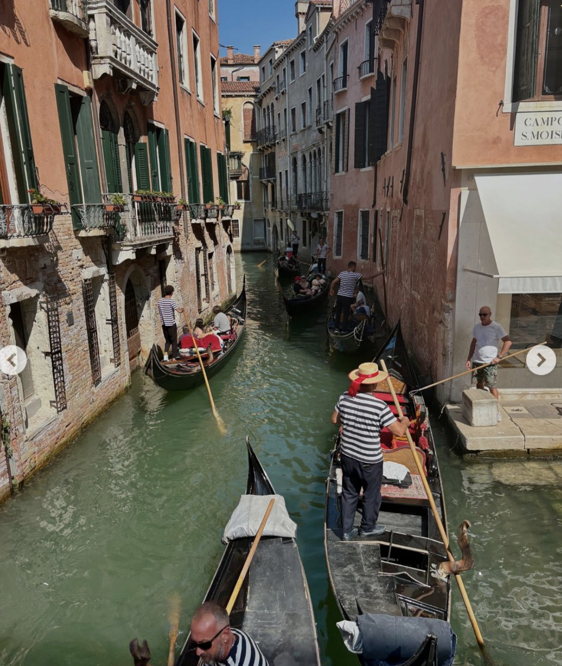 People maneuver gondolas through a narrow Venetian canal flanked by historic buildings