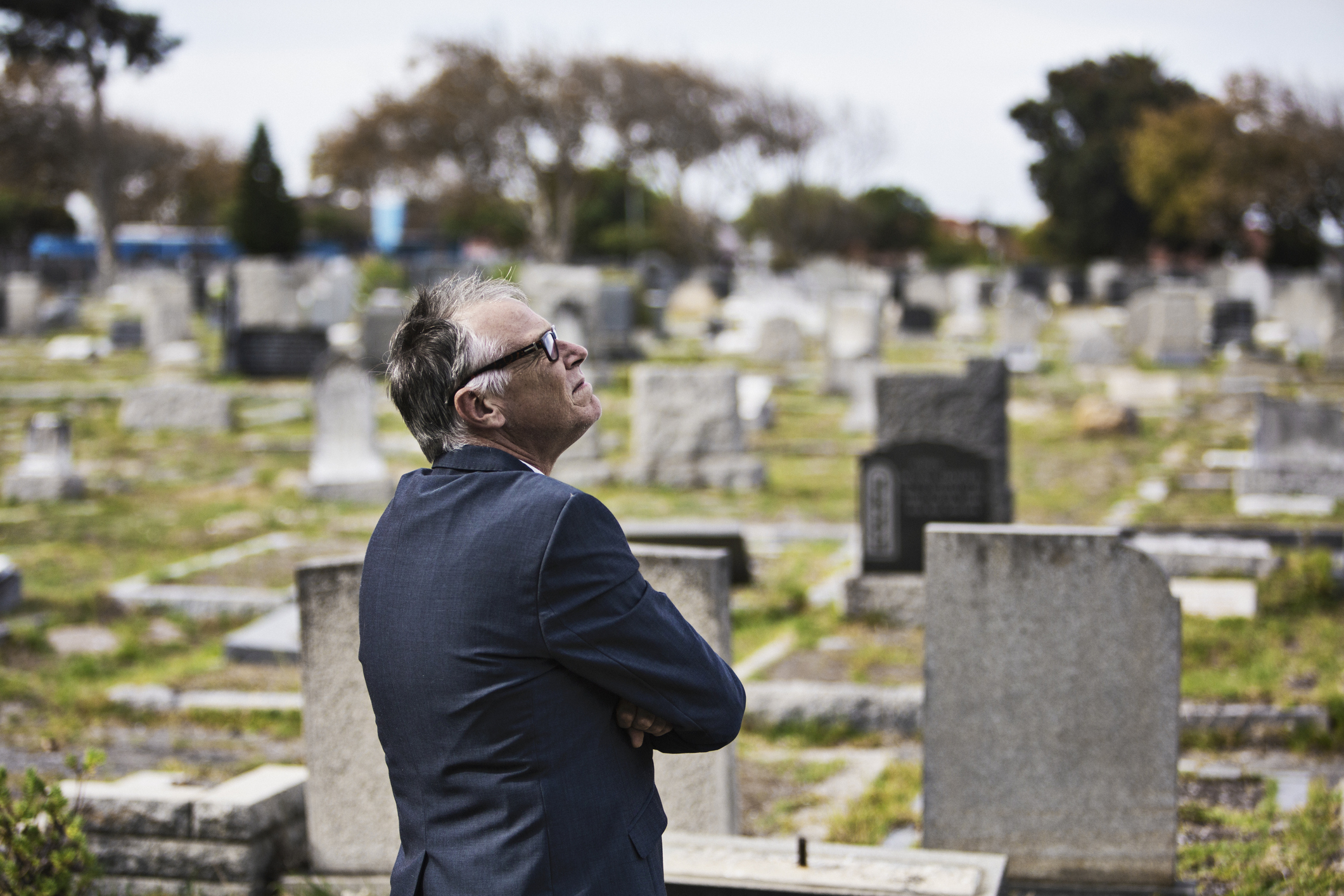 An older man in a suit looks contemplatively at the headstones in a cemetery