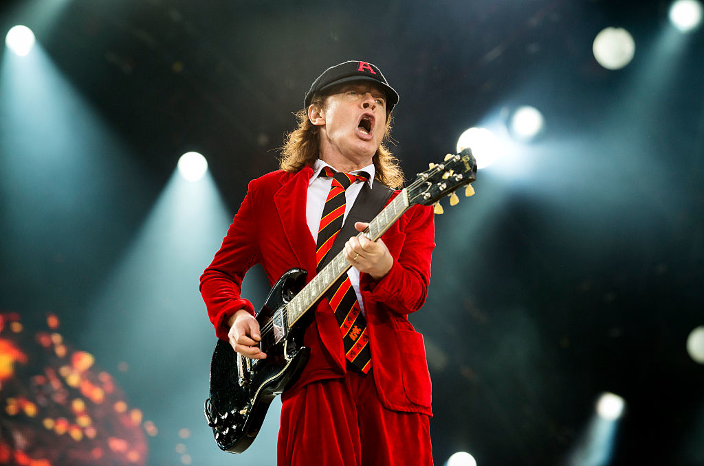 Angus Young performs energetically on stage in his signature schoolboy outfit, playing an electric guitar