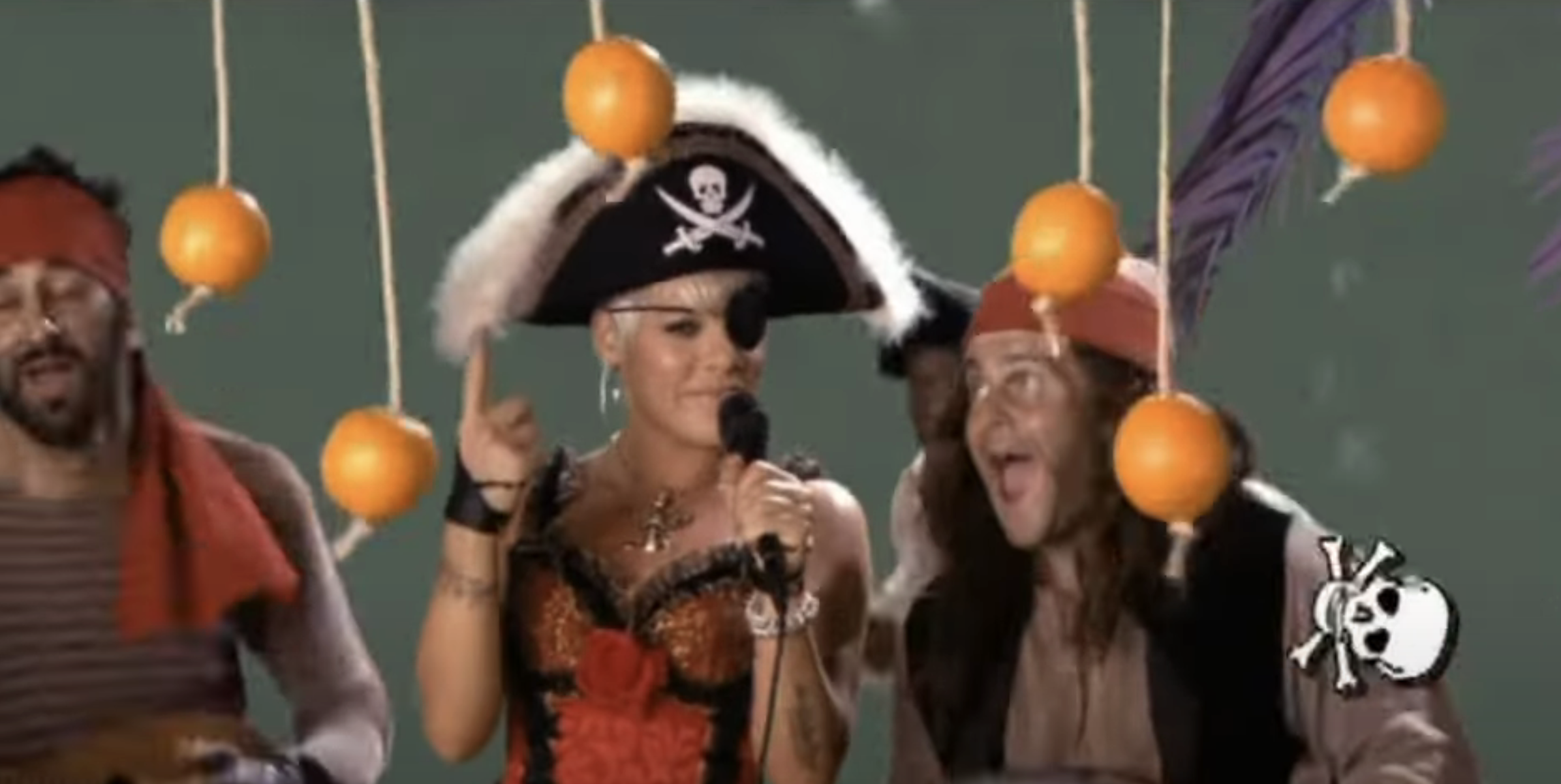 Pink dressed as a pirate, singing with pirates next to hanging oranges on stage