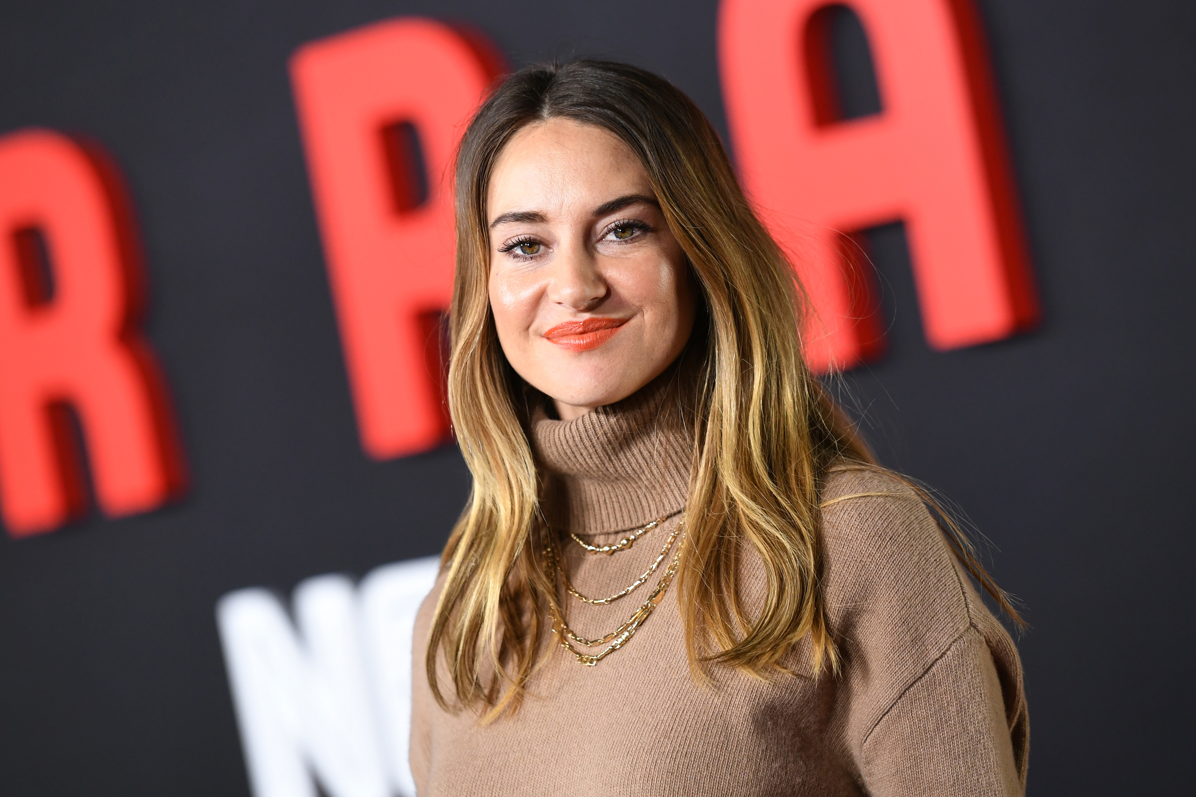 Shailene Woodley at a red carpet event, wearing a high-neck sweater and layered gold necklaces