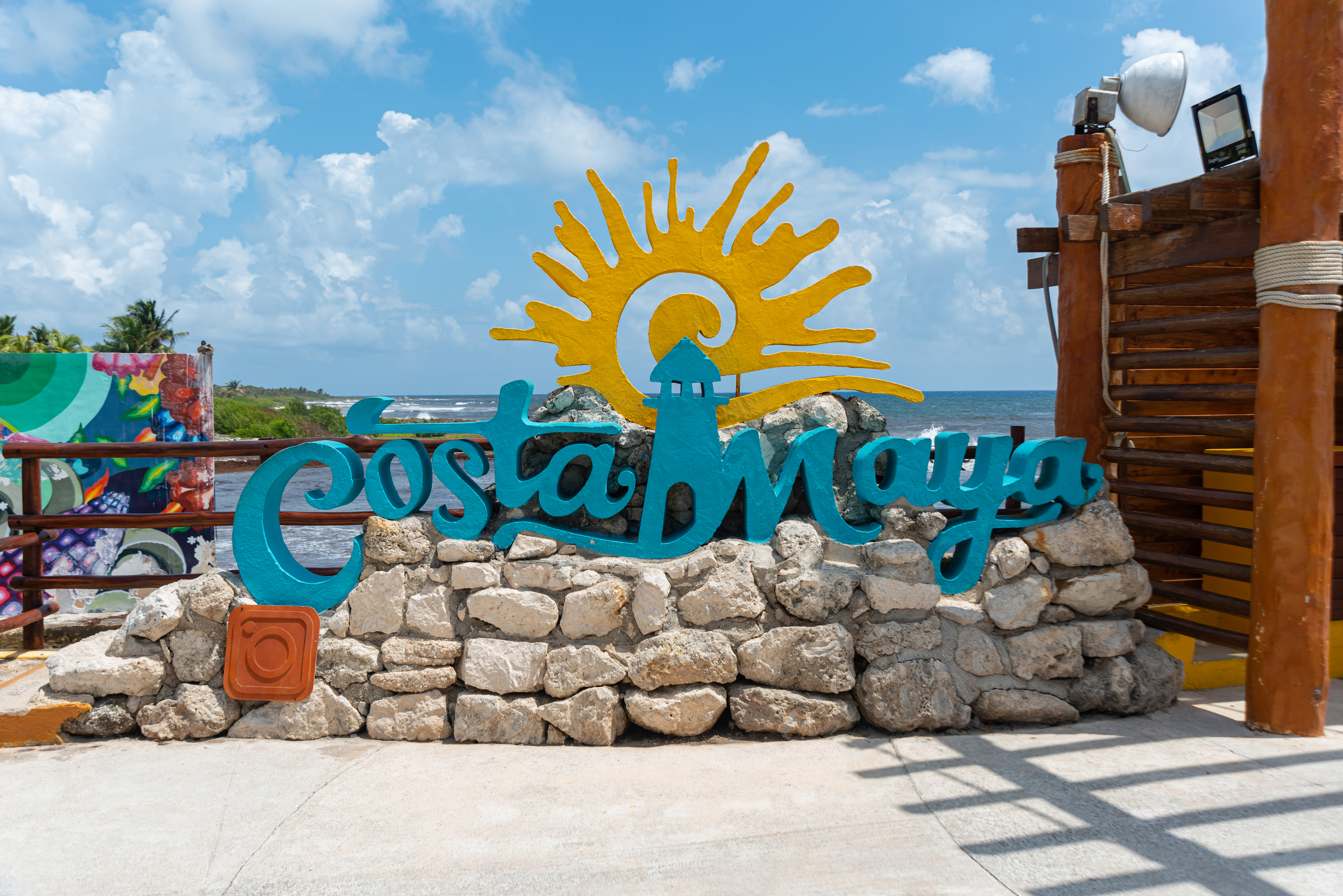 Sign for Costa Maya made of stone and brightly colored accents, with ocean and sky in the background