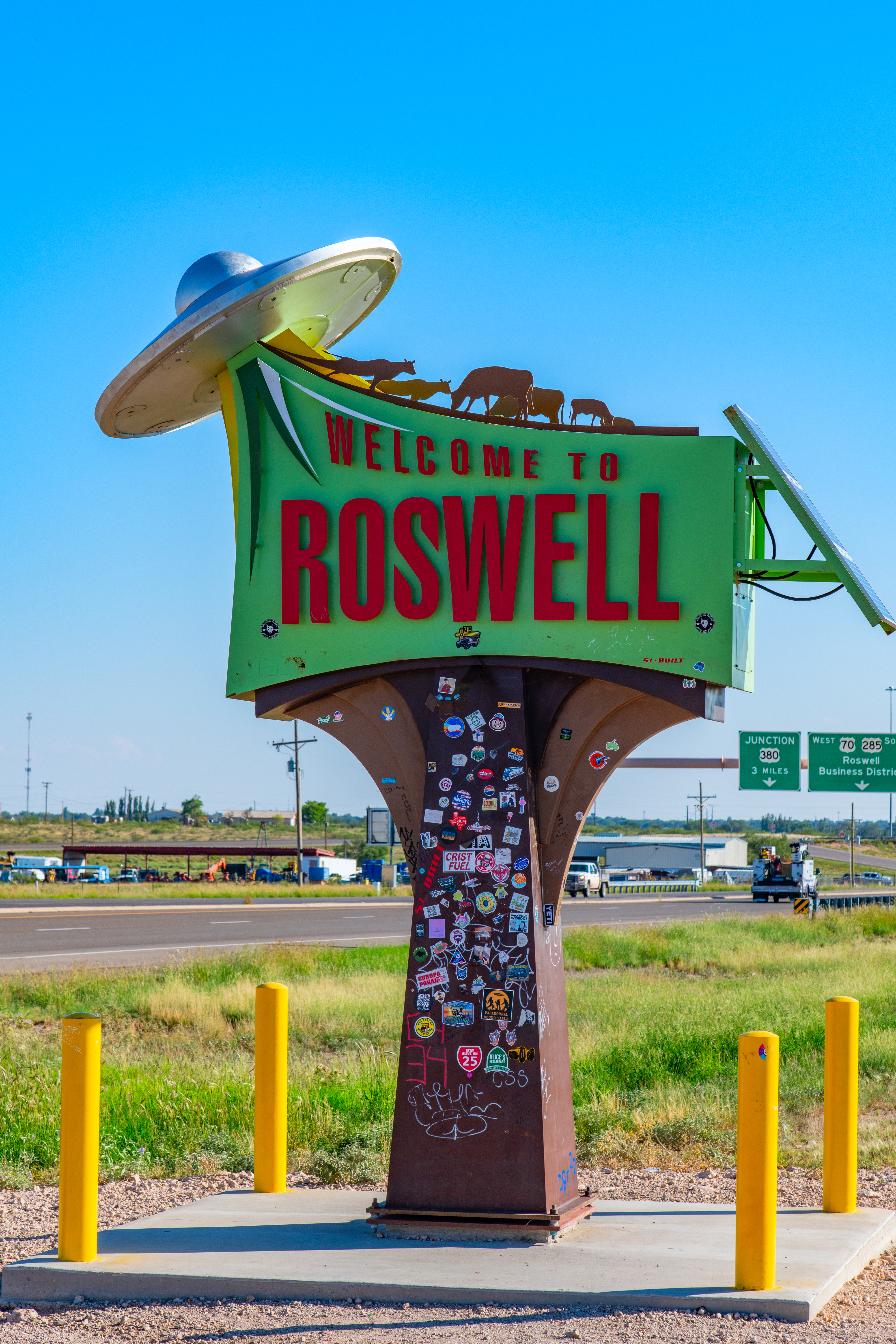 Roswell welcome sign featuring a UFO with animal silhouettes on top, with highway and grassy fields in the background