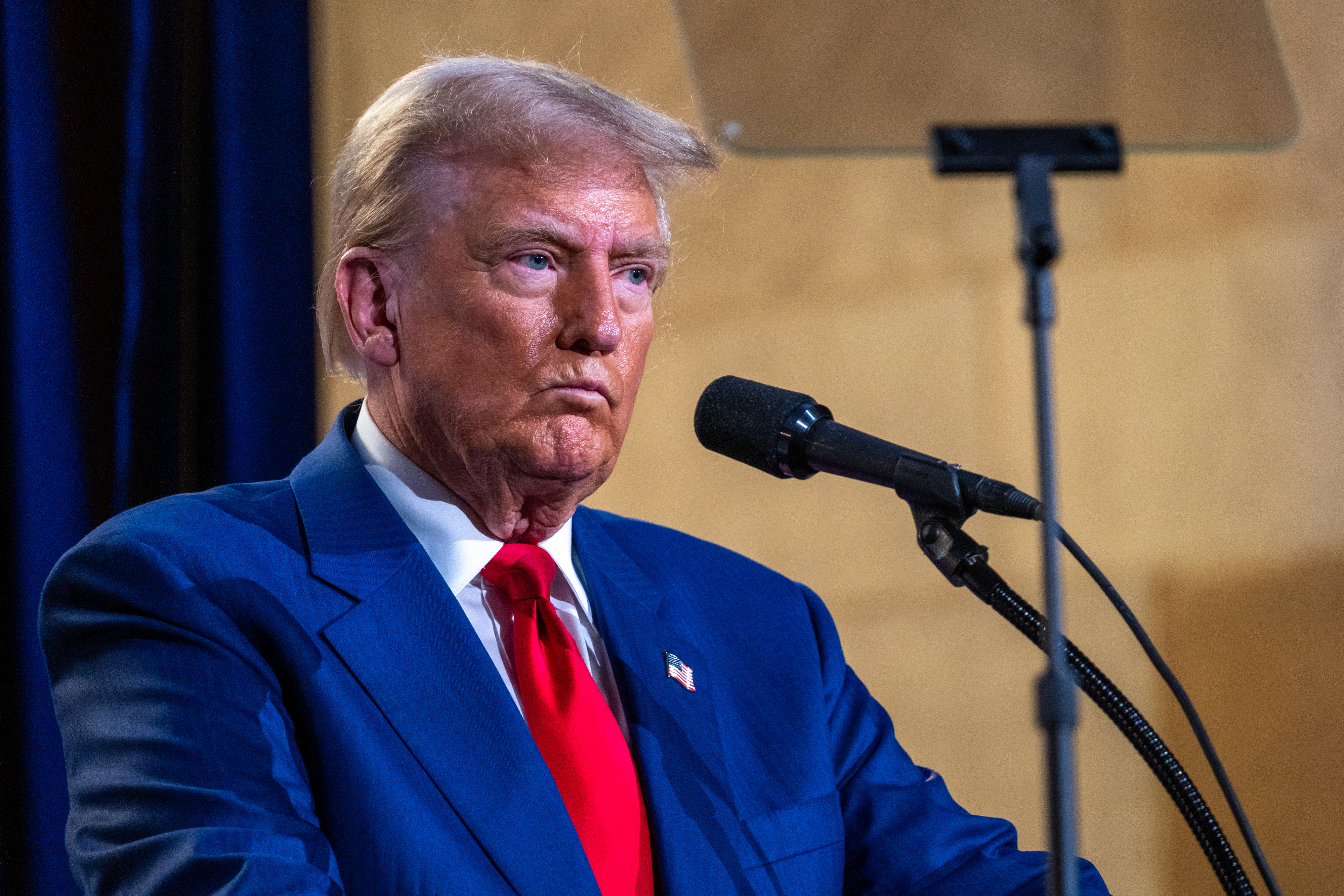 Donald Trump stands behind a podium, speaking into a microphone