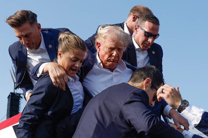 Donald Trump being assisted by Secret Service, appearing to steady him or help him down steps or a platform