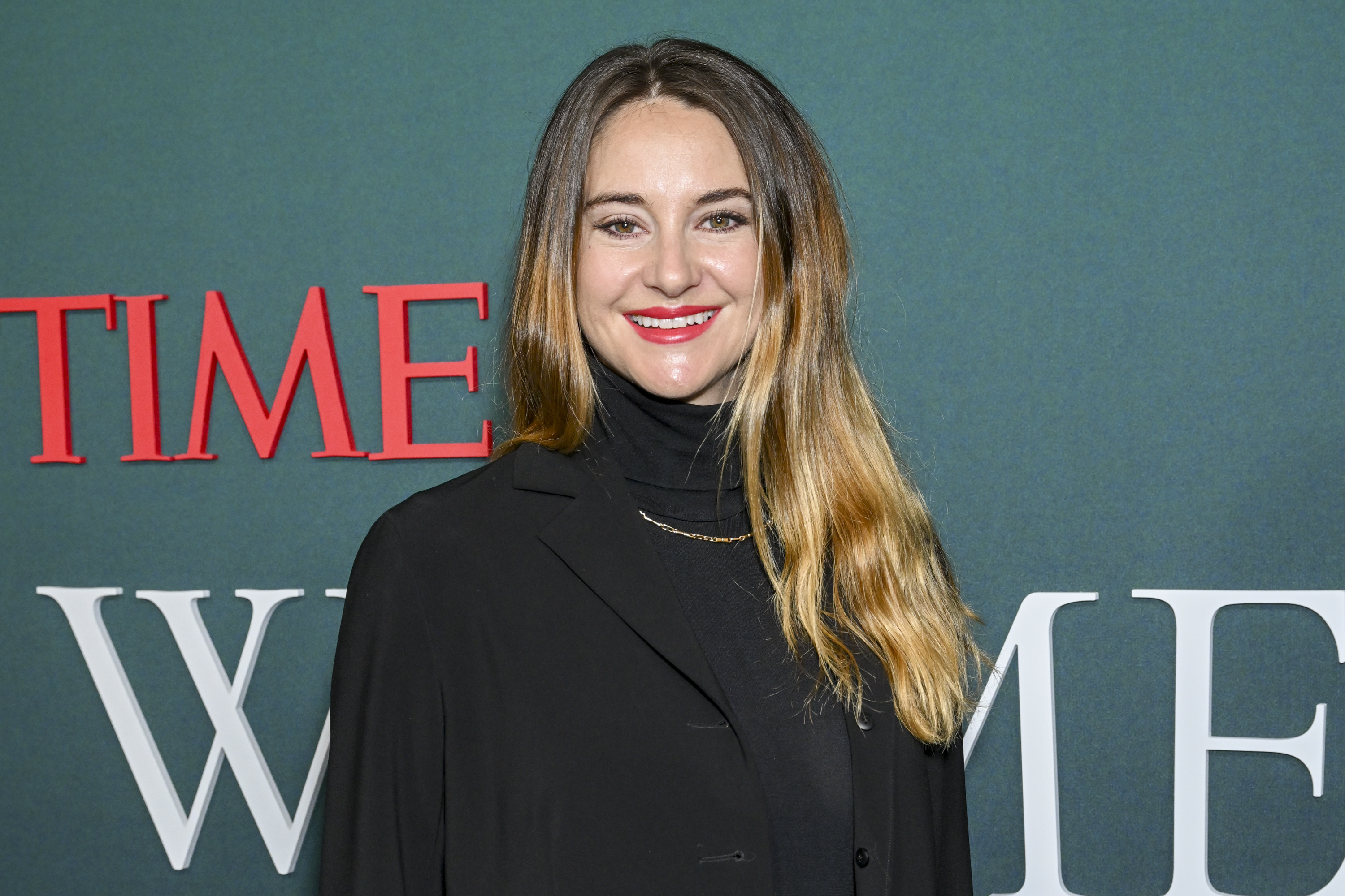 Shailene Woodley on the red carpet, wearing a dark blazer and turtleneck, smiling for photos