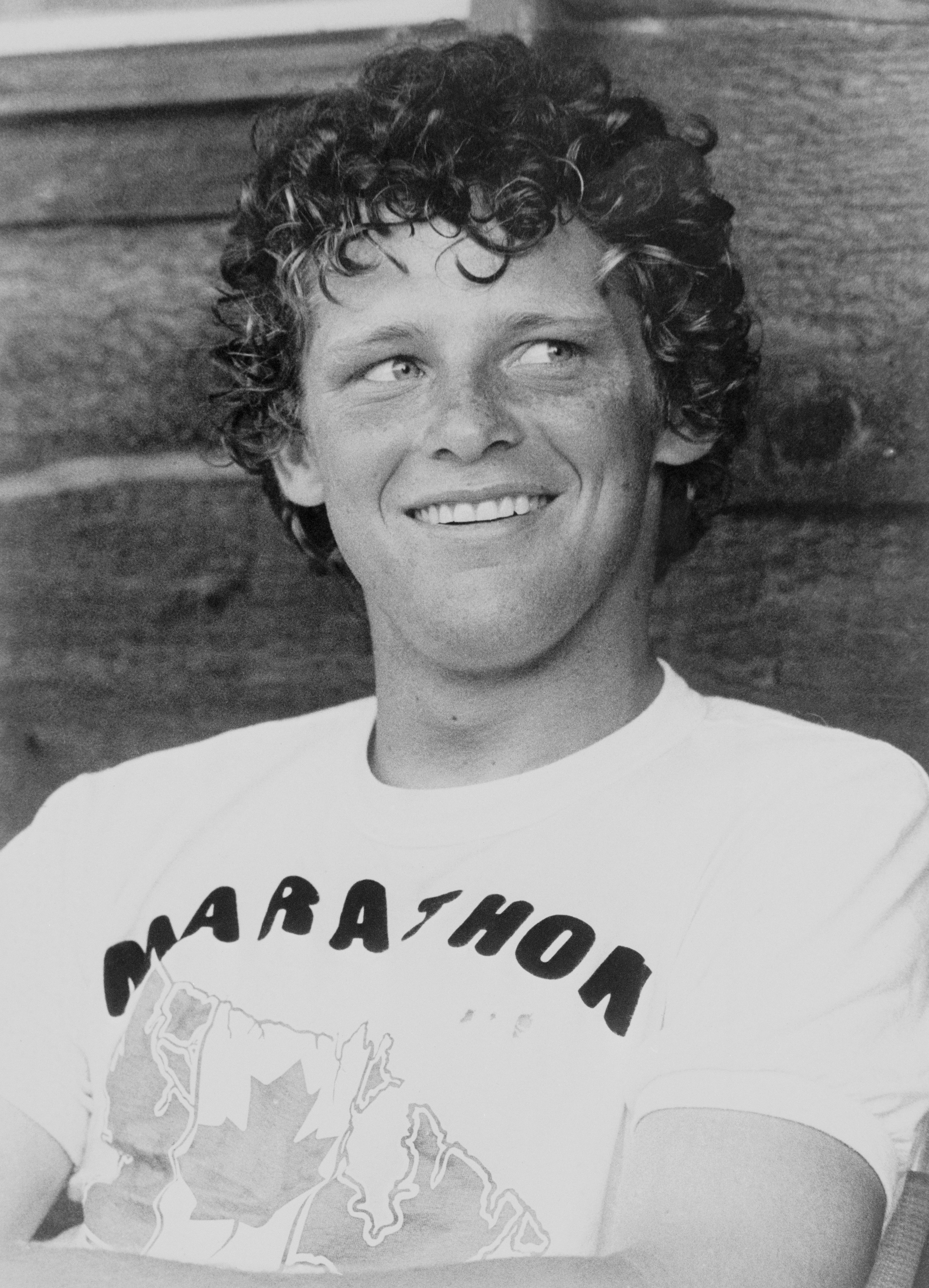 Terry Fox smiling while wearing a T-shirt with the word "Marathon" and a map design on it