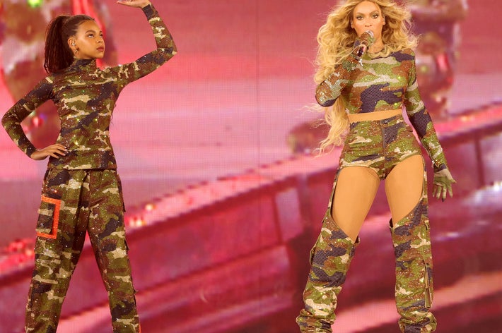 Beyoncé and Blue Ivy performing on stage in coordinated camouflage outfits. Beyoncé sings into a microphone while Blue Ivy holds up a fist