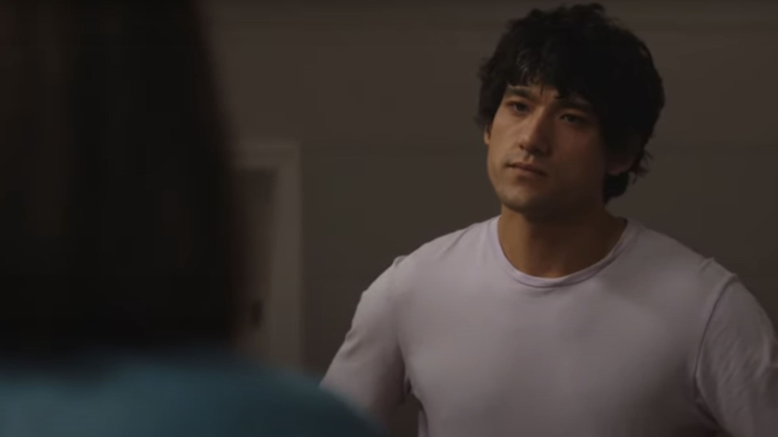 Jonny Lee stands indoors, looking concerned while talking to someone whose back is visible in the foreground